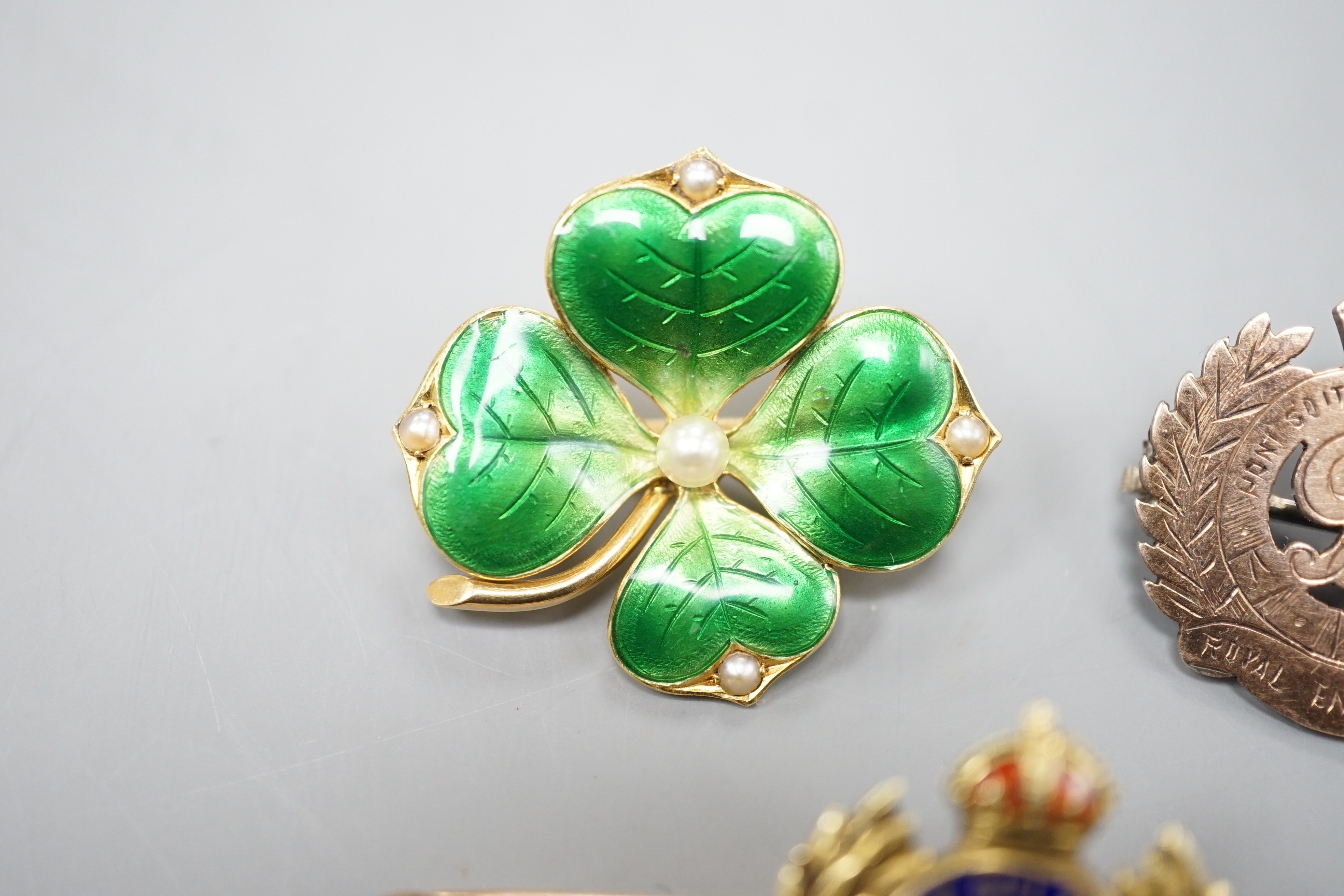 An early 20th century and two colour enamel set Royal Engineers sweetheart brooch, 5cm, gross 5.6 grams, an 18ct, seed pearl and green enamel clover brooch, 26mm, gross 6.2 grams and a sterling and yellow metal brooch.